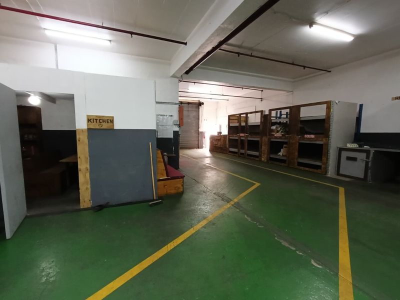 Spacious industrial utility area featuring painted concrete flooring, built-in storage shelving, and a large roller shutter door for easy access.