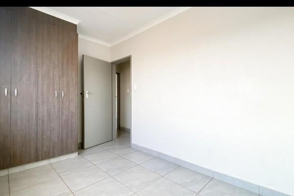A bright, empty bedroom featuring neutral tiled flooring and built-in wooden cupboards, offering a clean and versatile space.