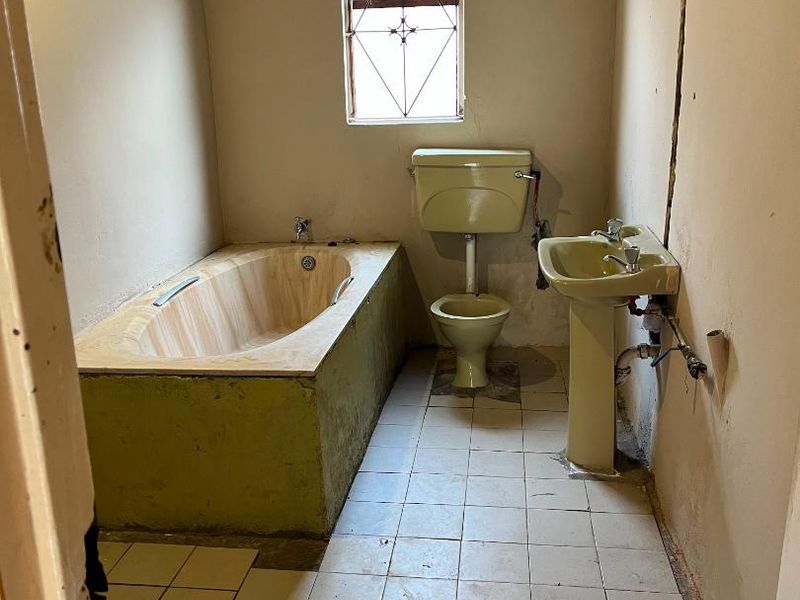 A bathroom in need of significant renovation, featuring original fixtures, unfinished walls, and exposed plumbing, offering a blank canvas for modernization.
