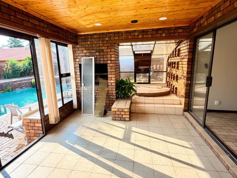 Covered patio area featuring exposed brick walls, timber ceiling, built-in braai, and a sunken jacuzzi, with direct access to the pool area.