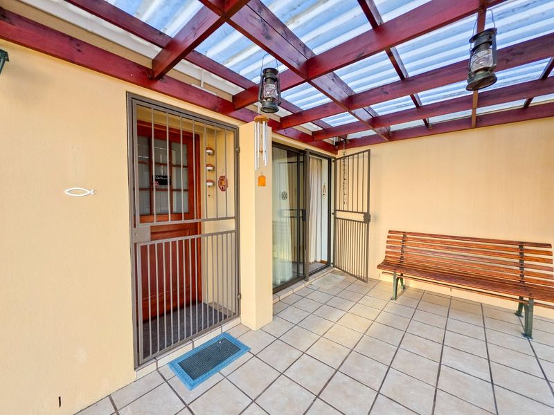 A covered patio area featuring a timber pergola with corrugated roofing, tiled flooring, and secure access points to the home.
