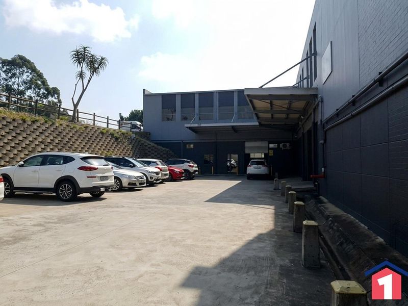 Industrial rear yard featuring a concrete surface, retaining wall, loading canopy, and roller shutter access point.