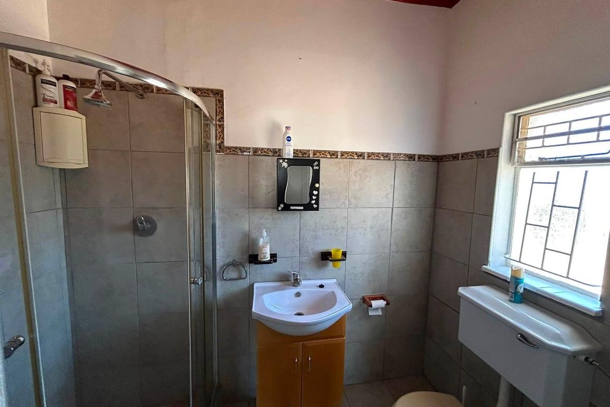 A functional bathroom featuring a shower enclosure, vanity basin, and toilet, with tiled finishes and a window providing natural light.