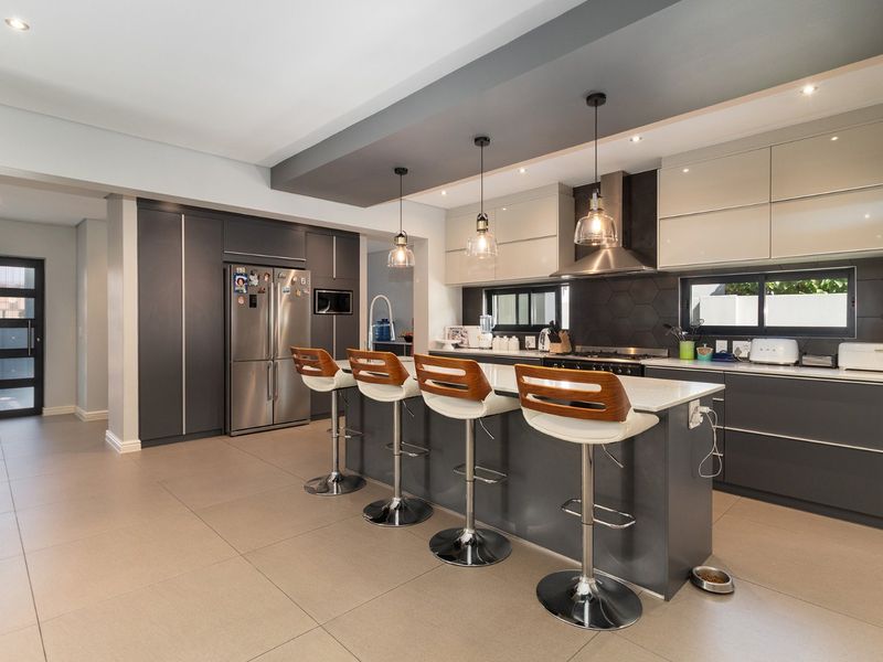 Modern, well-appointed kitchen featuring a large central island with breakfast bar seating, sleek cabinetry, stone countertops, and a stylish hexagonal tile backsplash.