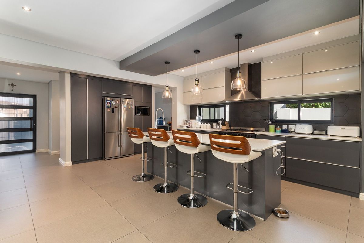 Modern, well-appointed kitchen featuring a large central island with breakfast bar seating, sleek cabinetry, stone countertops, and a stylish hexagonal tile backsplash.