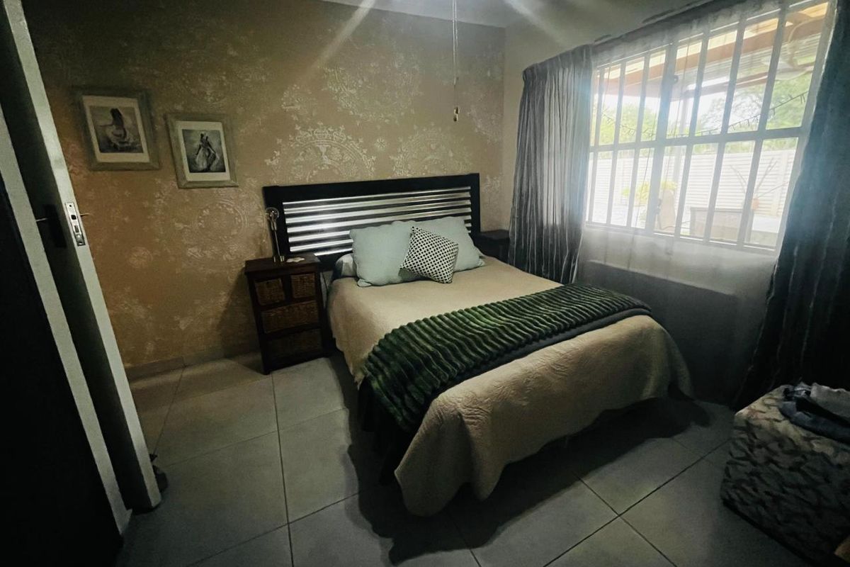 A bedroom featuring tiled flooring, a window with security bars, and a decorative feature wall.