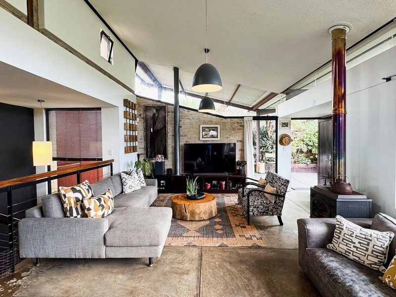 Spacious open-plan living area featuring a striking exposed stone wall, wood-burning fireplace, concrete floors, and high vaulted ceilings with clerestory windows.