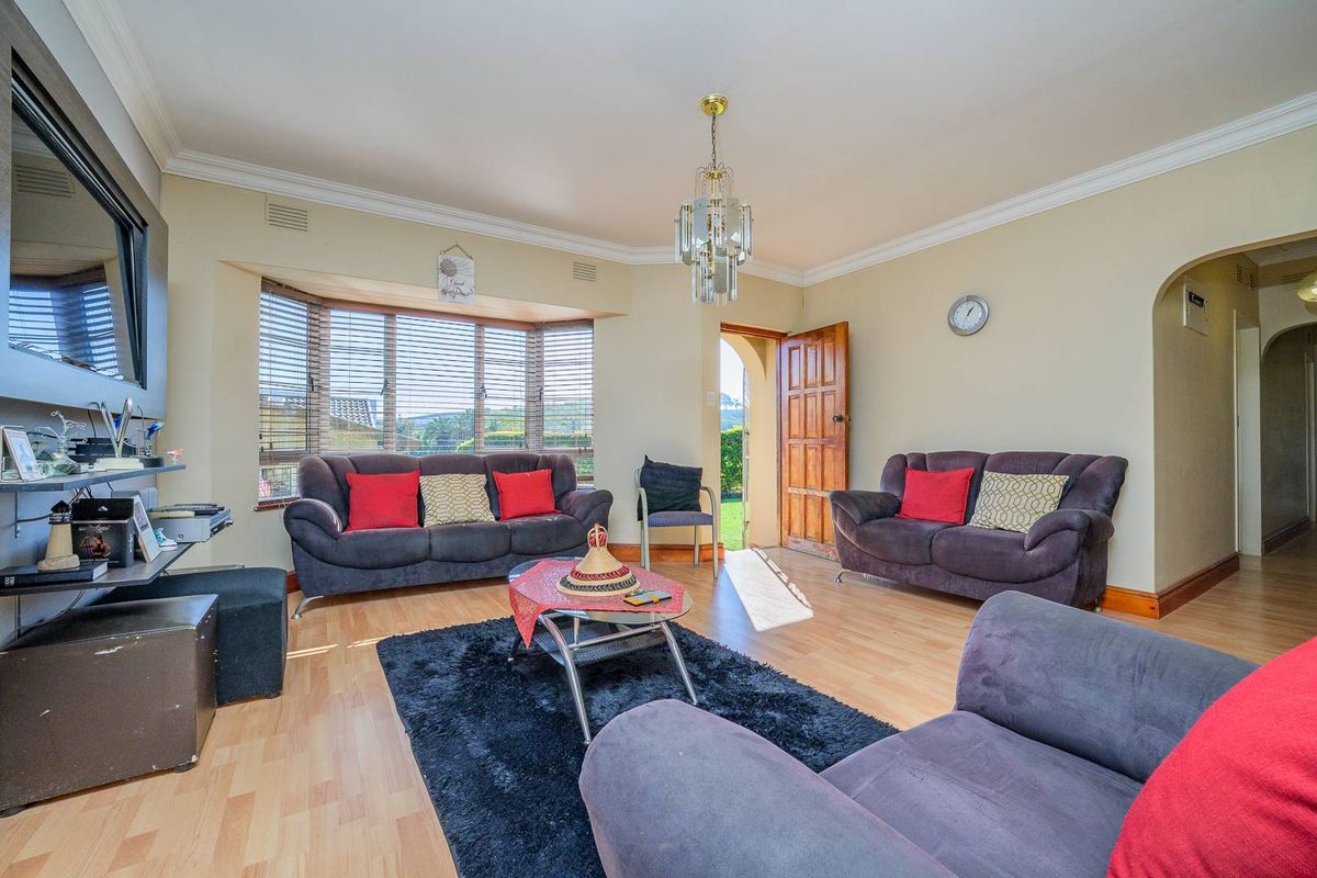 A spacious living room featuring a large bay window, laminate flooring, crown molding, and direct access to the exterior.