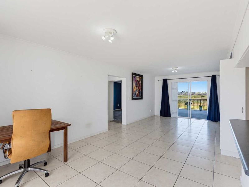 Spacious open-plan living area featuring neutral tiled flooring, ample natural light, and direct access to a balcony with scenic views.