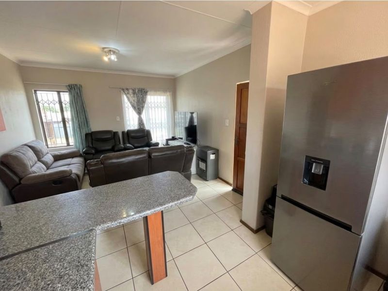 Open-plan living area featuring tiled flooring, a granite breakfast counter, and natural light through windows fitted with security bars.