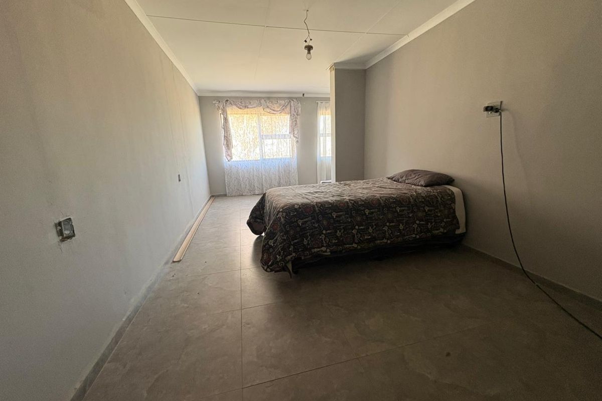 A spacious bedroom featuring tiled flooring, large windows, and basic lighting fixtures, currently presenting as a blank canvas for potential interior design updates.
