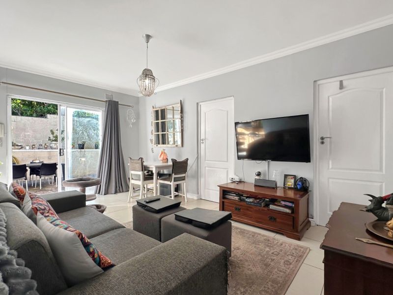 A well-maintained living room featuring tiled flooring, decorative ceiling cornices, and a sliding glass door providing access to an outdoor patio area.