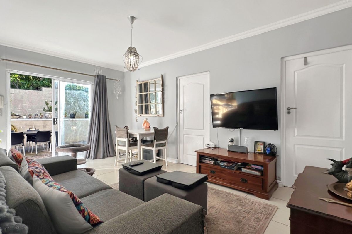A well-maintained living room featuring tiled flooring, decorative ceiling cornices, and a sliding glass door providing access to an outdoor patio area.