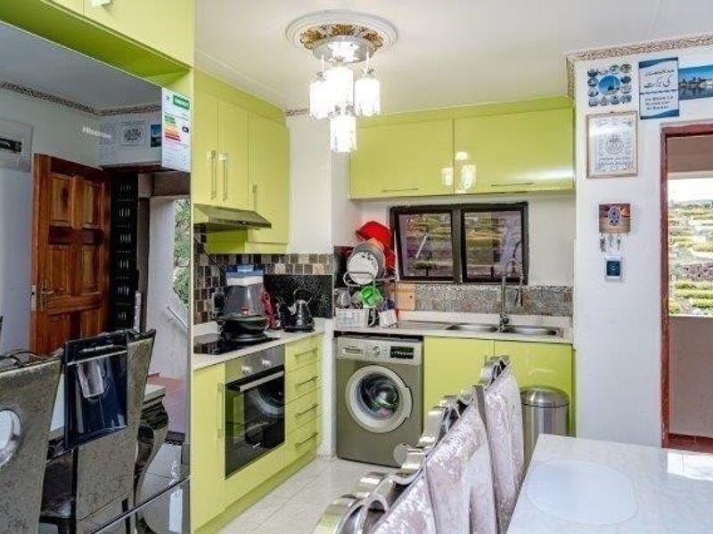 A compact kitchen featuring lime green cabinetry, built-in oven and hob, integrated washing machine, and a tiled backsplash with direct access to an outdoor area.