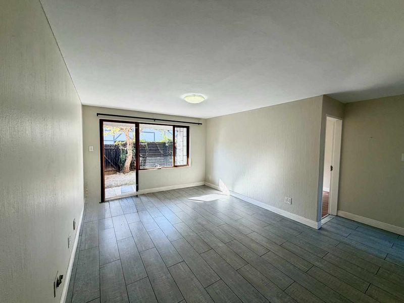 A bright, empty living room featuring modern grey tiled flooring and a sliding glass door providing direct access to the outdoor area.