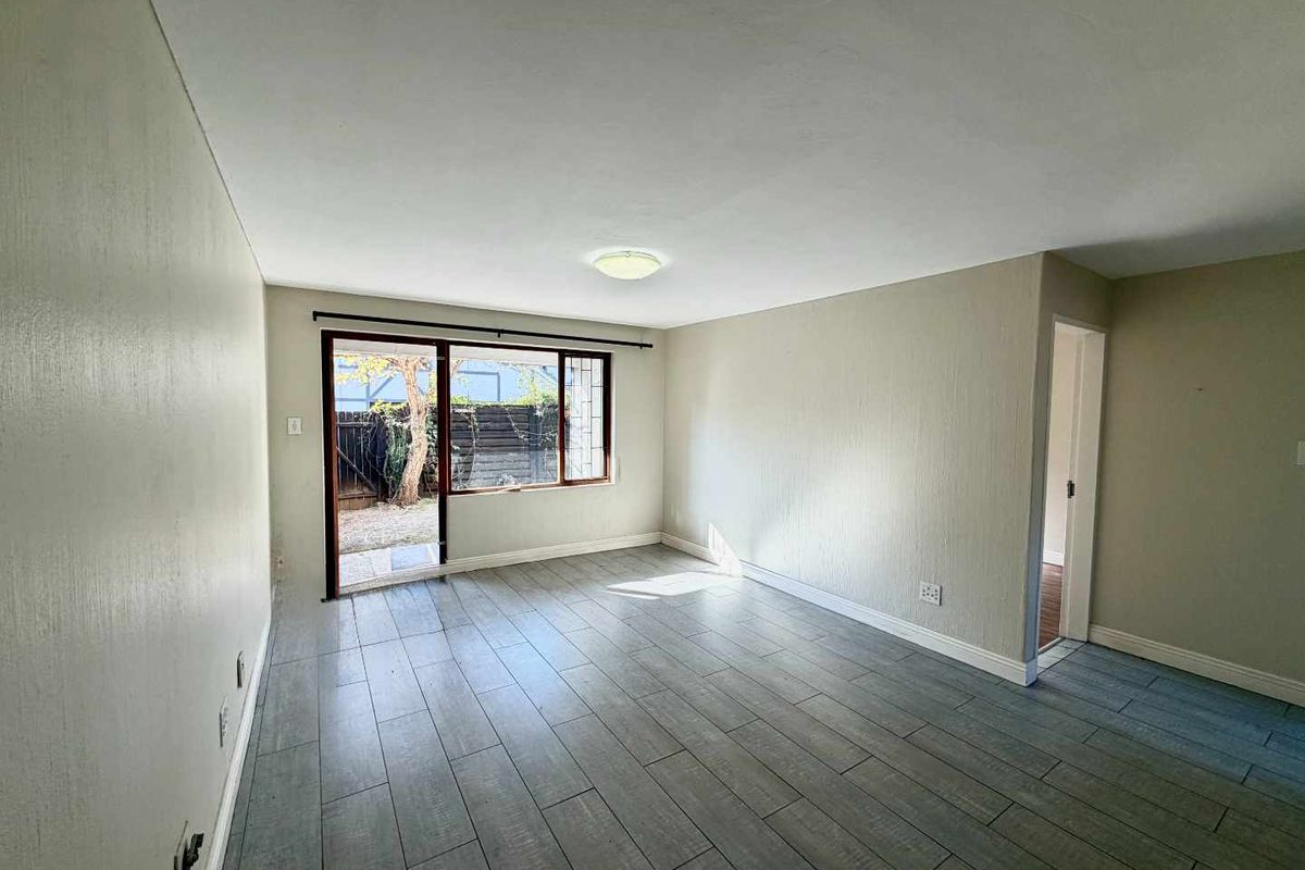 A bright, empty living room featuring modern grey tiled flooring and a sliding glass door providing direct access to the outdoor area.