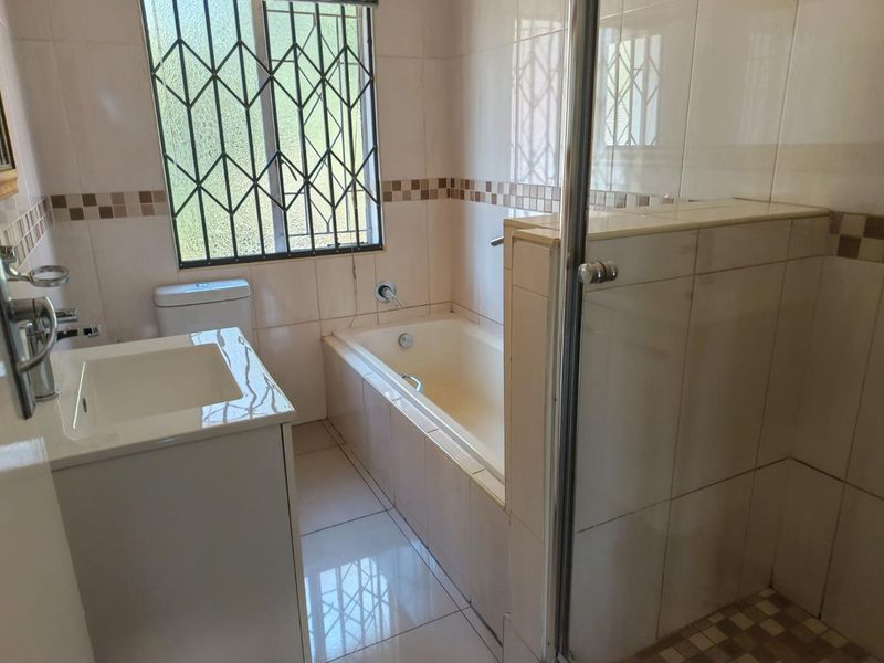 A functional bathroom featuring a built-in bathtub, separate glass-enclosed shower, vanity basin, and toilet, finished with neutral wall and floor tiles.