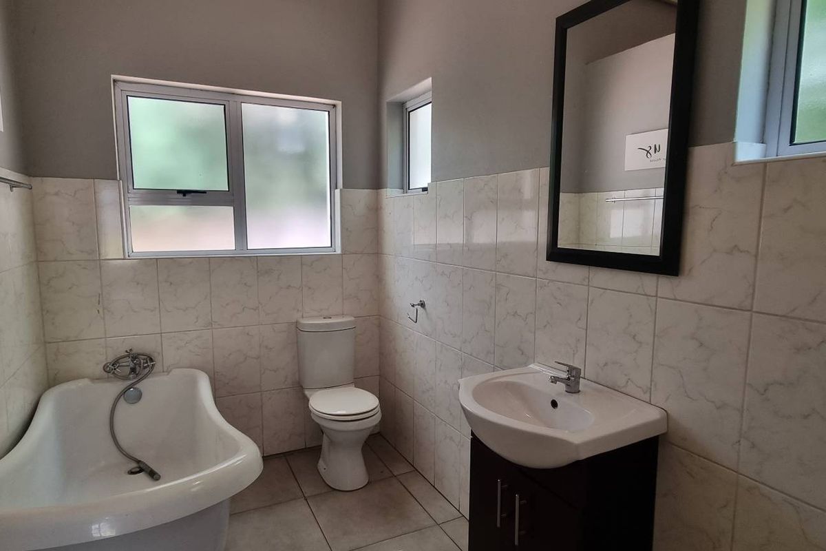 A functional bathroom featuring a classic clawfoot bathtub, a pedestal vanity with basin, and a standard toilet with tiled walls and flooring.