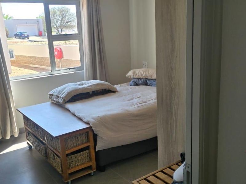A well-lit bedroom featuring tiled flooring, a built-in cupboard, and large aluminium-framed windows providing natural light.