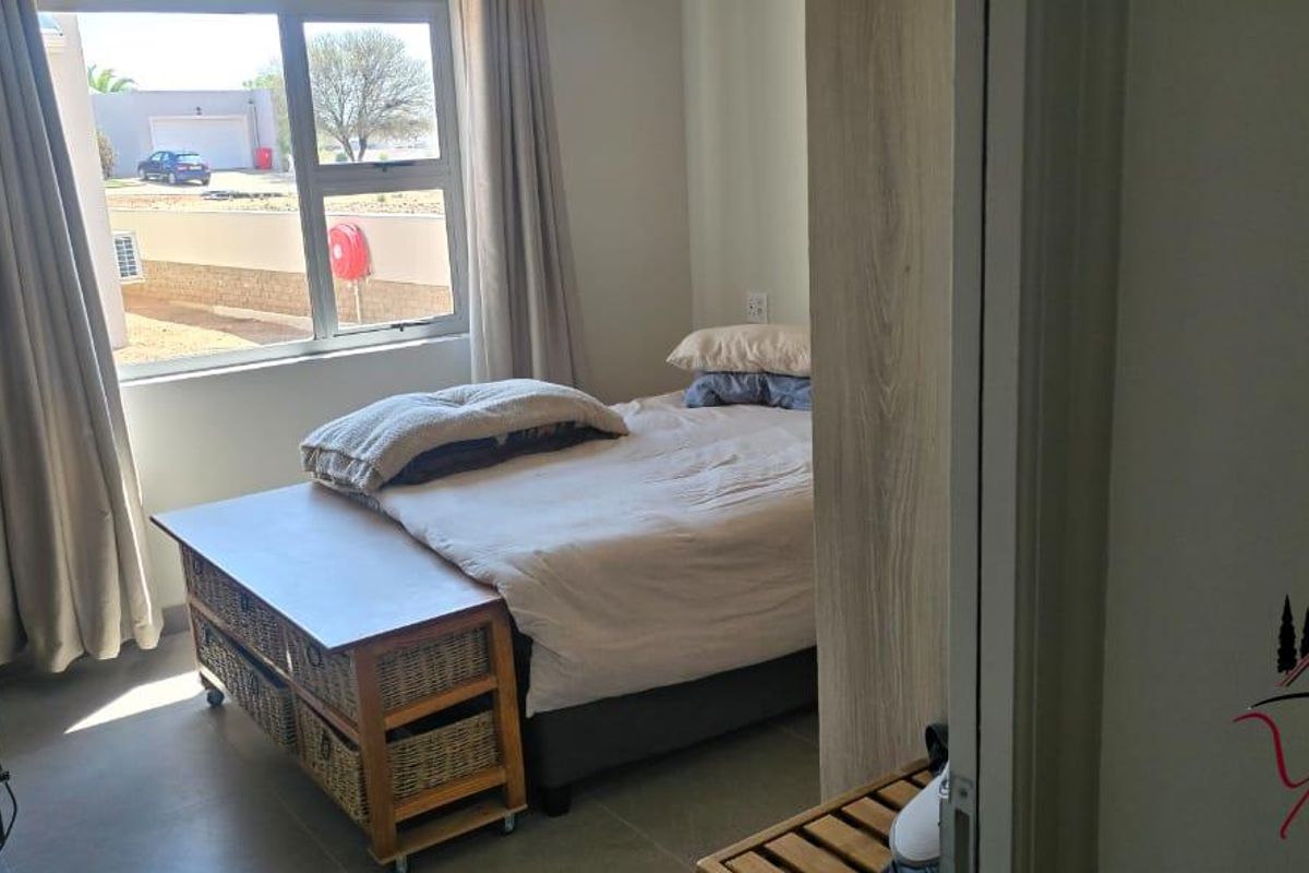 A well-lit bedroom featuring tiled flooring, a built-in cupboard, and large aluminium-framed windows providing natural light.