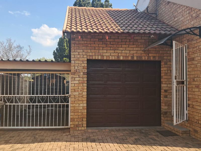 Exterior view of a brick-faced garage with a sectional door, paved driveway, and secure gated side access.