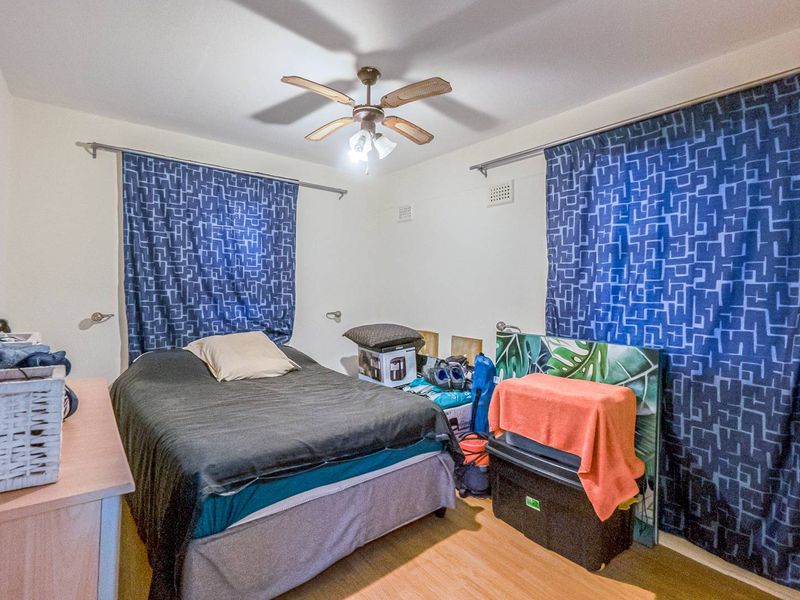 A bedroom featuring a ceiling fan, ventilation grilles, and laminate flooring, providing a functional space for rest.