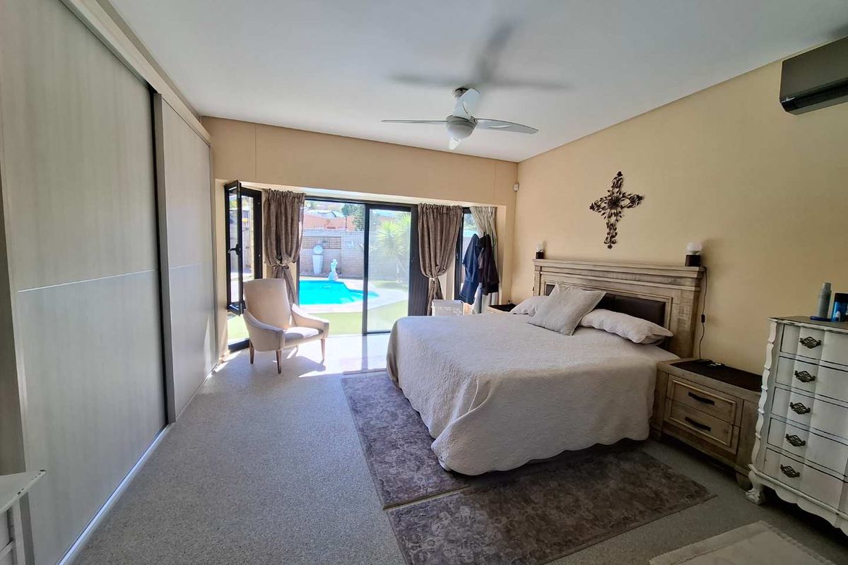 Spacious bedroom featuring built-in sliding wardrobes, a ceiling fan, air conditioning, and sliding glass doors providing direct access to the pool area.
