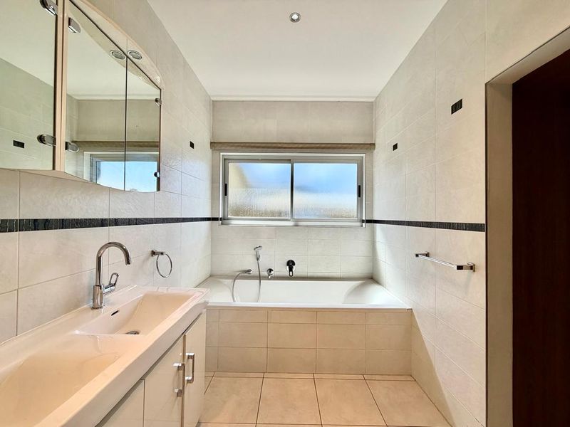 A clean, well-maintained bathroom featuring a built-in vanity with integrated basin, a tiled bathtub, and wall-mounted mirror cabinetry.