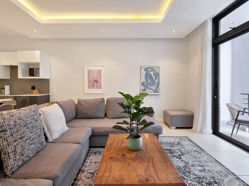 Modern open-plan living area featuring recessed cove lighting, sleek tiled floors, and seamless access to an outdoor balcony through large sliding glass doors.