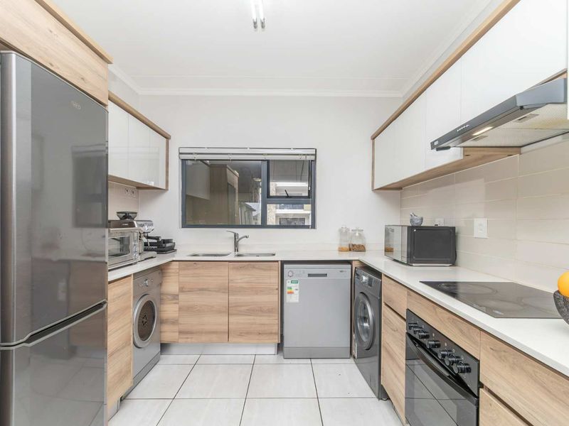 Modern galley-style kitchen featuring light wood-tone cabinetry, white stone countertops, tiled backsplash, and integrated appliances including an electric hob and oven.