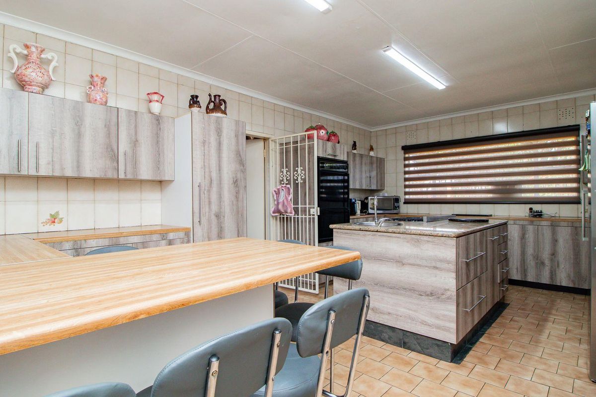 Spacious kitchen featuring wood-look cabinetry, a central island with integrated sink, breakfast bar, and tiled flooring.