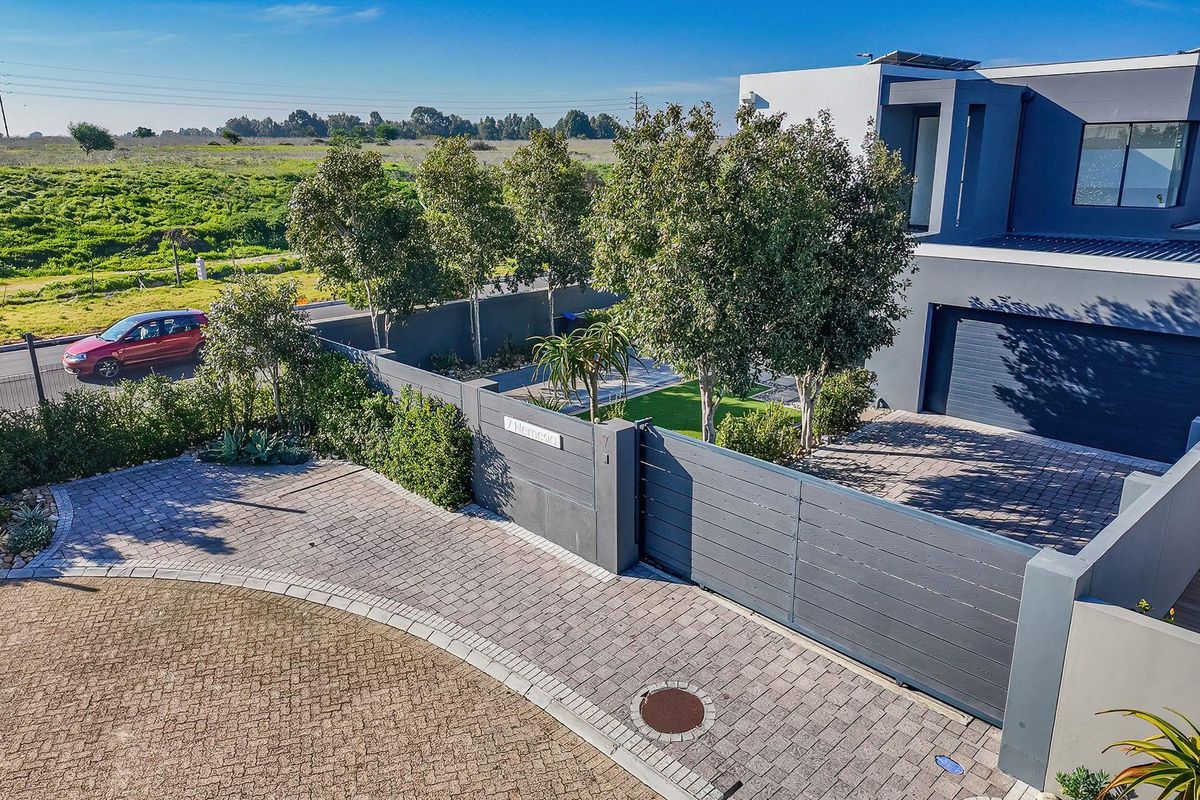 Aerial view of a modern residential property featuring a paved driveway, secure gated entrance, landscaped garden, and contemporary architectural facade.