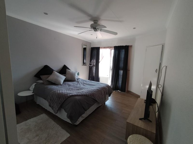 A well-lit bedroom featuring tiled flooring, a ceiling fan, recessed lighting, and a sliding glass door providing access to the exterior.