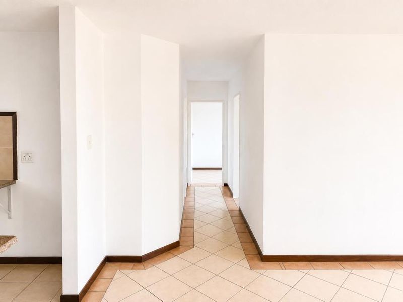A bright, empty hallway featuring neutral tiled flooring and clean white walls, providing access to adjacent rooms within the apartment.