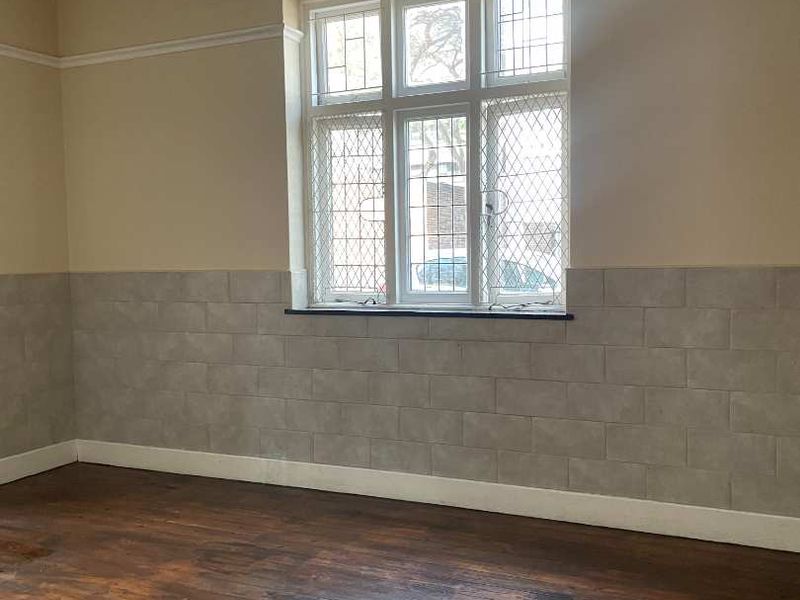 An empty living room featuring original timber flooring, leaded glass windows, and tiled wainscoting, offering a blank canvas for renovation.