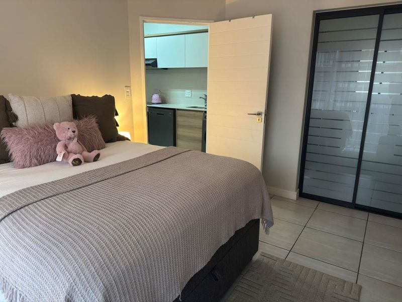A well-maintained bedroom featuring tiled flooring and a built-in sliding door wardrobe, with a direct view into the adjacent kitchen area.