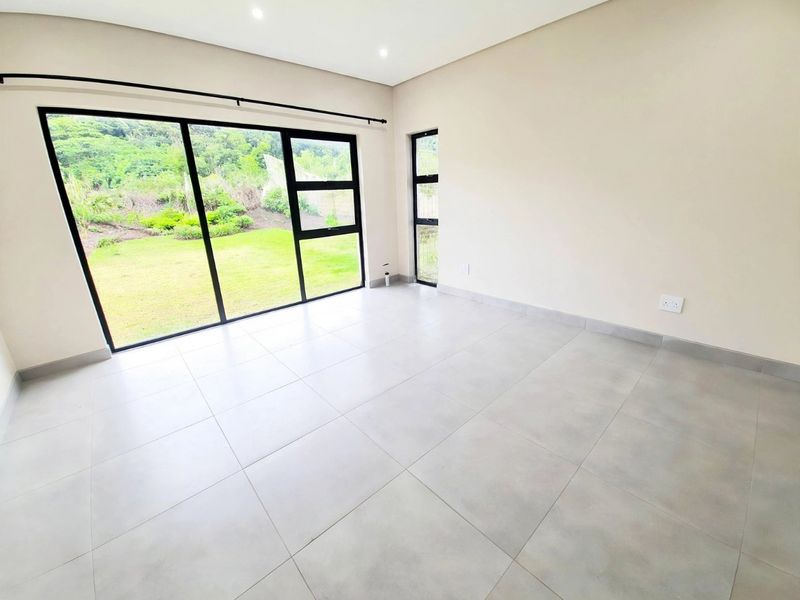 A bright, modern, and empty bedroom featuring large aluminium sliding doors that open to a garden view, complemented by neutral tiled flooring.