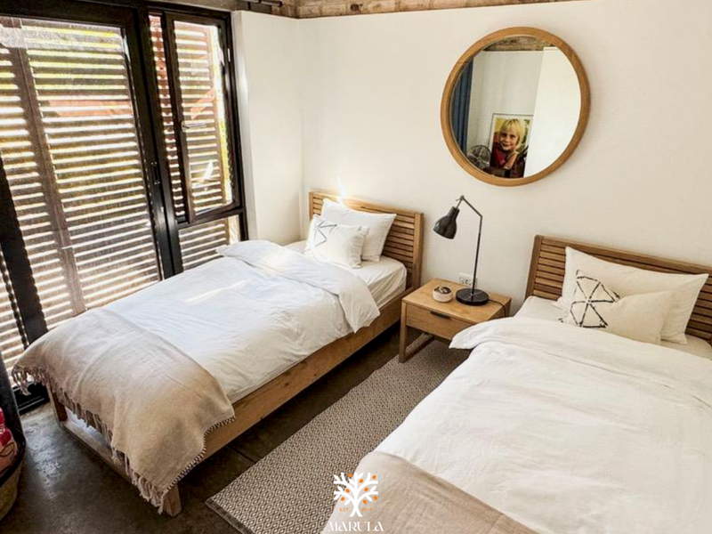 A well-lit bedroom featuring exposed brickwork, polished concrete floors, and large sliding glass doors with integrated louvre shutters for natural light control.