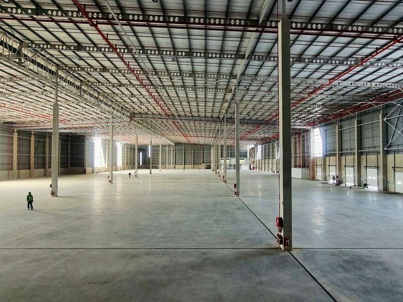 A vast, open-plan industrial warehouse space featuring high ceilings with exposed steel trusses, fire sprinkler systems, and polished concrete flooring.
