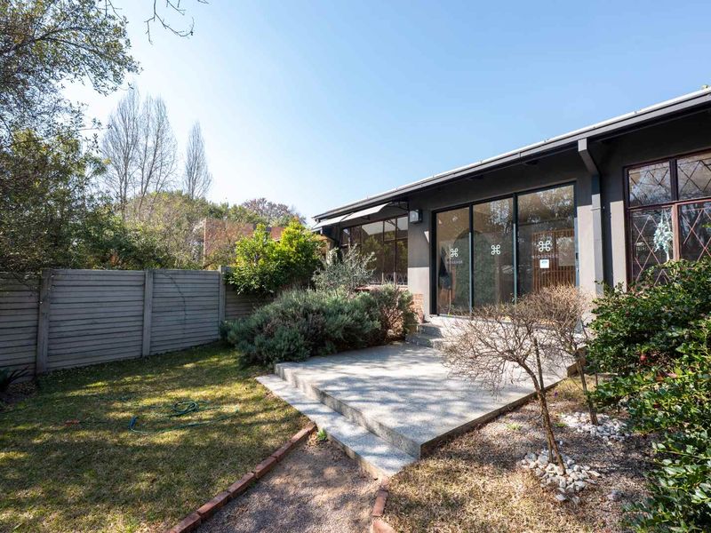 Rear view of the property featuring a concrete patio, sliding glass doors, and a well-maintained garden with a boundary wall.