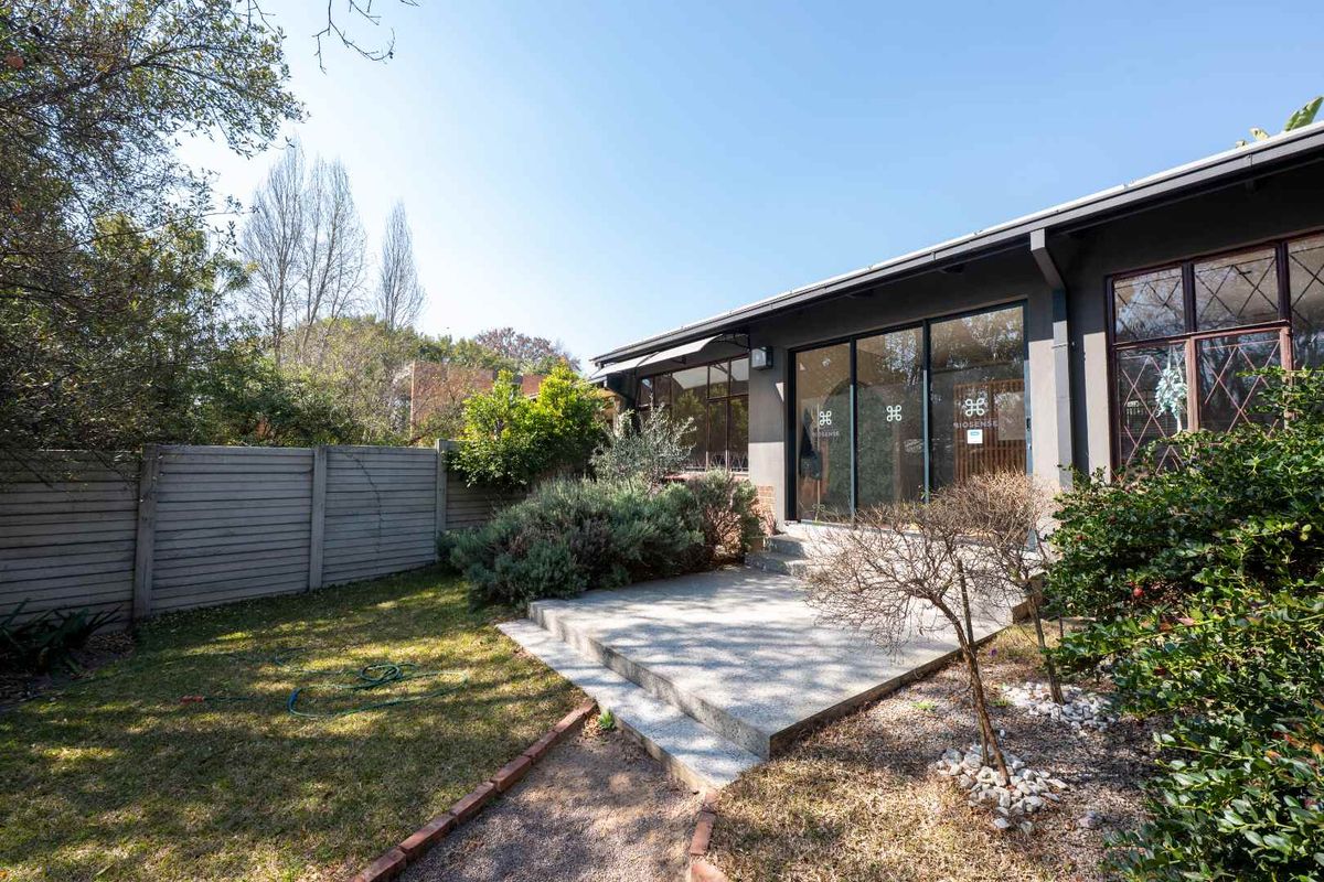 Rear view of the property featuring a concrete patio, sliding glass doors, and a well-maintained garden with a boundary wall.