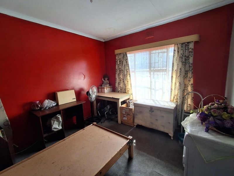 A bedroom featuring red painted walls, window security bars, and visible ceiling water staining, requiring cosmetic updates and repairs.