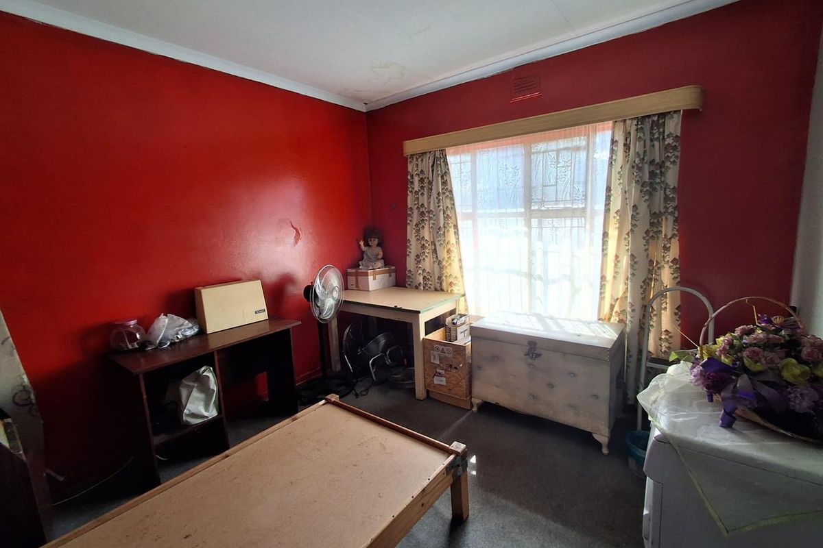 A bedroom featuring red painted walls, window security bars, and visible ceiling water staining, requiring cosmetic updates and repairs.