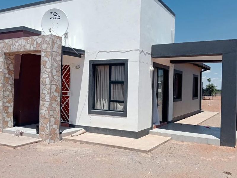 Modern single-story residential home featuring a stone-clad entrance, clean white and dark exterior finishes, and a covered patio area.