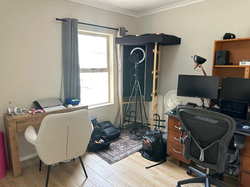 A functional bedroom space featuring tiled flooring and a window, currently utilized as a home office and recording area.