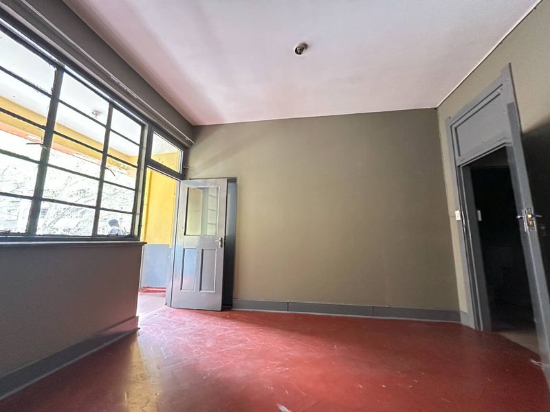 An empty living area featuring painted concrete floors, steel-framed windows, and direct access to an outdoor balcony space.
