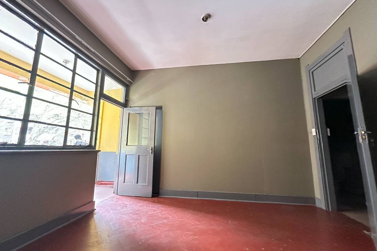 An empty living area featuring painted concrete floors, steel-framed windows, and direct access to an outdoor balcony space.