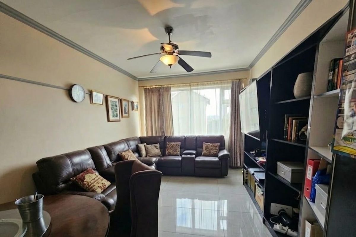 A living room featuring tiled flooring, crown molding, and a central ceiling fan, providing a functional and comfortable space.