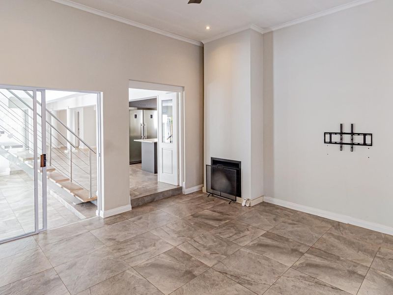 Spacious living area featuring large format floor tiles, a built-in fireplace, and direct access to an adjacent staircase and kitchen area.