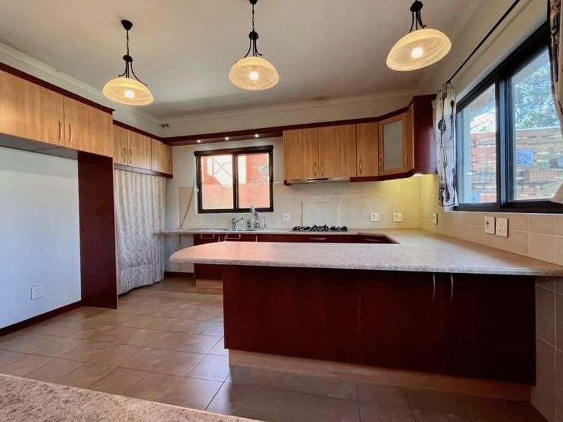 A spacious kitchen featuring built-in cabinetry, laminate countertops, a gas hob, and tiled flooring, offering a functional layout with ample storage space.